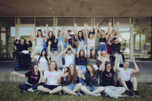 Auf dem Bild sieht man eine Gruppe vieler Menschen, welche ihre Arme in die Luft strecken und lachen.