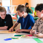 Drei Jungen sitzen an einem Tisch und basteln gemeinsam mit buntem Papier.