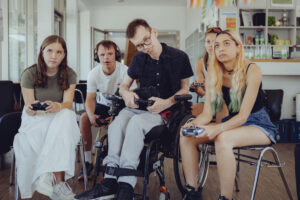 Auf dem Bild sieht man fünf Personen, welche zusammen ein Videospiel spielen.