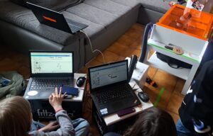 Auf dem Bild sind Jugendliche abgebildet, die an Laptops verschiedene Motive entwerfen. Ein Laptop ist mit dem Lasercutter verbunden. Der Lasercutter ist etwa 70 cm breit, 50 cm tief und 25 cm hoch. Im inneren befindet sich der eigentliche Laser und das Schienensystem. Der Deckel ist orange und verhindert, dass Laserstrahlen nach außen gelangen.