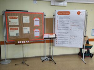 Auf der linken Seite sind Info-Platten zu Hate Speech an einer Pinnwand angebracht. Auf der rechten Seite können Besucher:innen mit Klebepunkten angeben, wie sie Hassrede entgegnen würde.