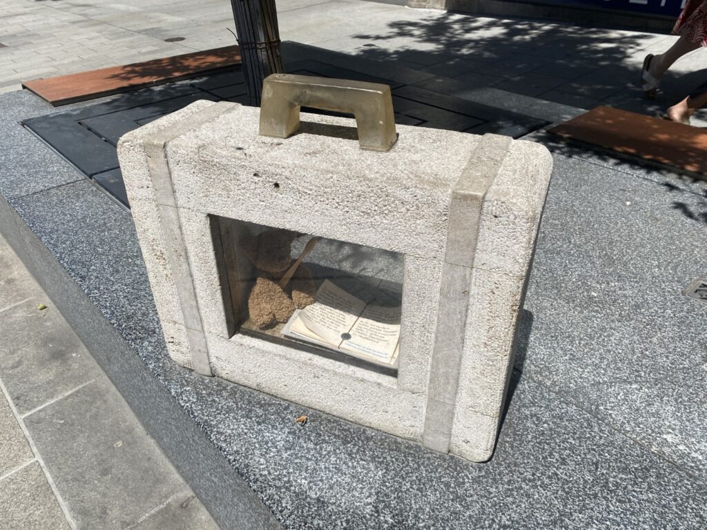 Das Bild zeigt einen Koffer aus Beton mit einer Glasscheibe. Dahinter ist ein Teddybär zu erkennen.