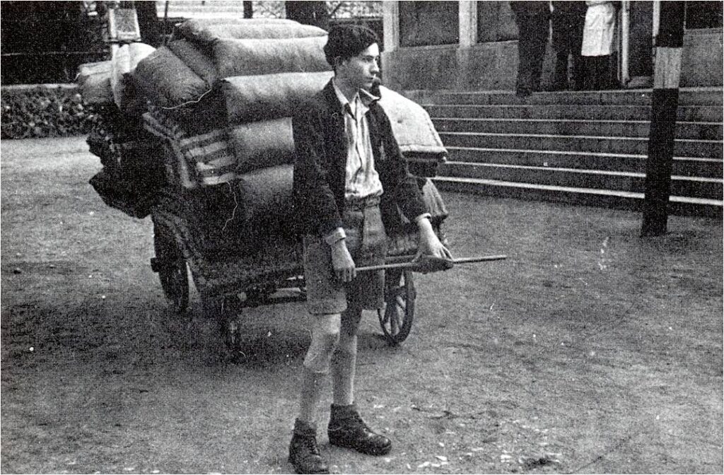 Auf dem Bild der Gestapo vom 25.04.1942 ist Max Ansbacher als Jugendlicher abgebildet. Er steht vor einem Karren mit Gepäckstücken während der Deportation von jüdischen Mitbürgern von der Sammelstelle Platzscher Garten in Würzburg.